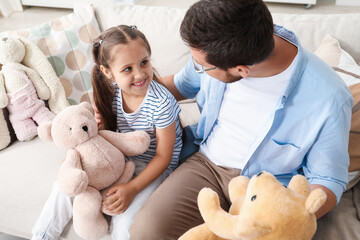 Father and his daughter playing with teddy bears on sofa at home