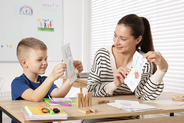 Cute boy learning letters with teacher at desk in school