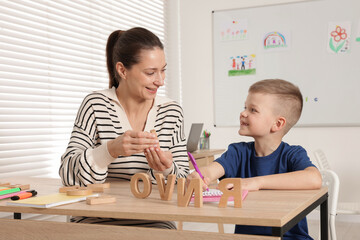 Cute boy learning letters with teacher at desk in school