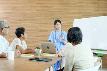 Group of elderly people discussing with female caregiver at a nursing home, reflecting social...