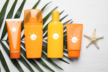 Sunscreen products, palm leaf and sea star on white background, top view. Bottles and tubes with...