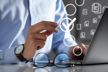 Man putting check mark on virtual screen while working on laptop at table, closeup