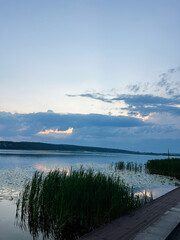 Calm lake view at sunset with reeds and cloudy sky