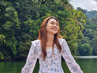 Beautiful female tourist in a casual dress enjoying the view of the lake on a boat with a happy...