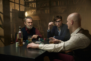 A group of men enjoying time playing poker in a dimly lit bar while sipping on drinks