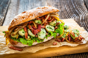 Takeaway sandwich with broad beans, fried bacon and caramelized onion on wooden table