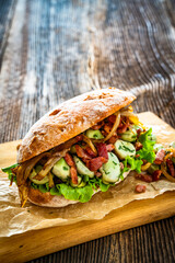 Takeaway sandwich with broad beans, fried bacon and caramelized onion on wooden table