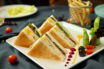 Club sandwich served with french fries on a white plate in a restaurant background 