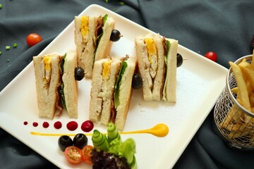 Club sandwich served with french fries on a white plate in a restaurant background 