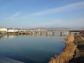 Fototapeta premium A scenic view of a city, a truss bridge crossing the Kiso River, and the snow-capped Mount Ibuki in the distance in Japan.