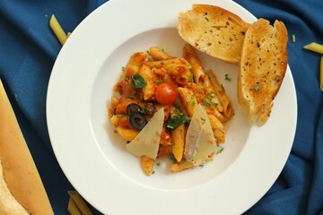 Penne pasta with cheese, cherry tomato and garlic bread on a white plate