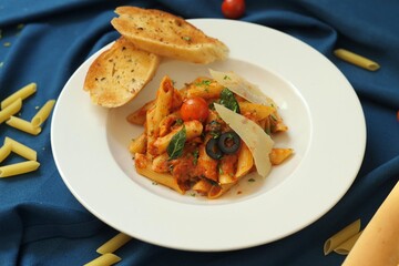 Penne pasta with cheese, cherry tomato and garlic bread on a white plate
