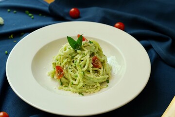 Pesto spaghetti pasta with bread and basil on white plate