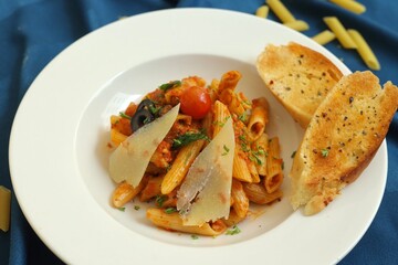 Penne pasta with cheese, cherry tomato and garlic bread on a white plate