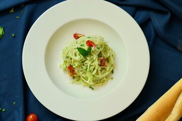 Pesto spaghetti pasta with bread and basil on white plate