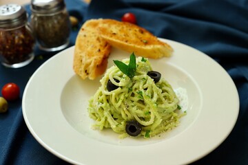 Pesto spaghetti pasta with bread and basil on white plate