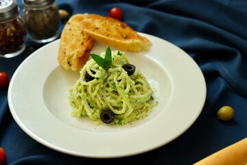 Pesto spaghetti pasta with bread and basil on white plate