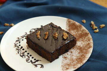 Walnut chocolate brownie decorated with walnut and chocolate syrup placed on a white plate