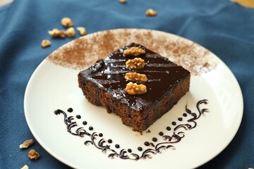Walnut chocolate brownie decorated with walnut and chocolate syrup placed on a white plate