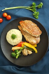 Grilled chicken with vegetables on the side served on a fancy white plate in a restaurant or cafe background 