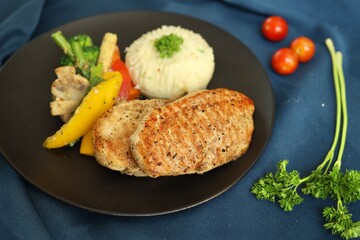 Grilled chicken with vegetables on the side served on a fancy white plate in a restaurant or cafe background 