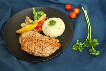 Grilled chicken with vegetables on the side served on a fancy white plate in a restaurant or cafe background 