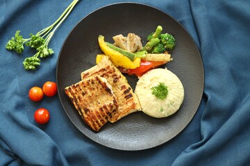 Grilled chicken with vegetables on the side served on a fancy white plate in a restaurant or cafe background 