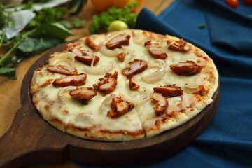 Pizza with chicken pieces and cheese on it places in a pizzeria background