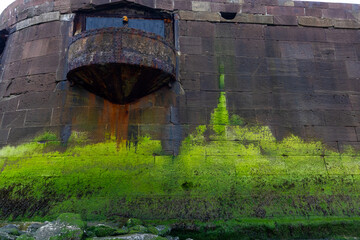 Detailed view of Perch Rock Fort's moss-covered wall, featuring a rusted observation post and vivid...