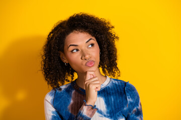 Portrait of a fashionable young woman pondering against a bright yellow background, showcasing...