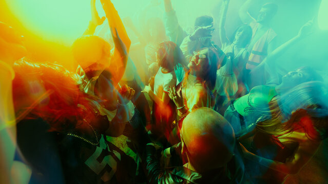Vibrant crowd dancing at a party with colorful motion blur effects. Concept of concert, party, music, rhythm.