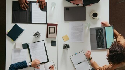 High angle shot of three unknown businessmen and young woman holding work meeting at white table with open laptop, documents and notebooks
