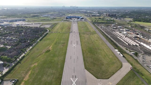 Aerial drone shot flying high above decommissioned Downsview Airport runway, approaching Rogers Stadium in Toronto under clear daytime sky