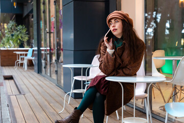 Elegant Caucasian lady in a coat walks across the autumn city and talks on the phone, staying in touch while enjoying a weekend break. Mid shot