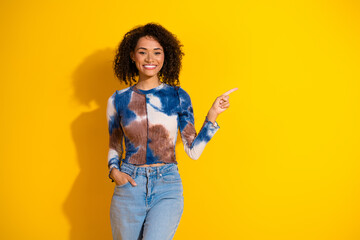 Stylish young woman in casual clothes pointing with a cheerful expression against a vibrant yellow...