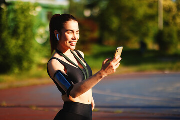 Young sportswoman using smartphone and wearing wireless earphones during training in a park