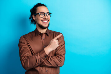 Cheerful man in brown formal shirt pointing sideways with a lively smile against a vibrant turquoise background