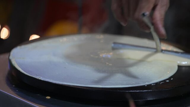 Chef skillfully spreads crepe batter on a hot plate, creating a thin, even layer for a perfect crepe