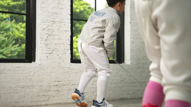 Before the tournament day, a boy and girl dressed in fencing gear are rehearsing in gym