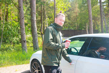 Man in Sports Jacket Enjoying Morning Coffee Outdoors by Car in Nature and Opening Car Door. Road trip