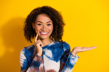 Confident young woman in a stylish tie-dye print shirt smiling against a vibrant yellow background...