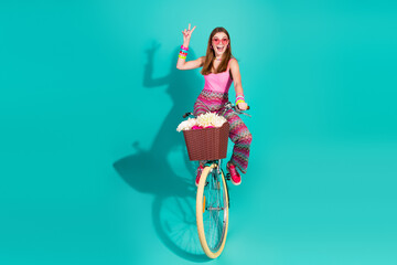 Retro-styled girl on a teal background riding a bicycle with a basket of flowers, expressing joy...
