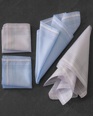 Folded blue and beige handkerchiefs arranged on a dark background, showcasing classic men's accessories in a clean, elegant style.