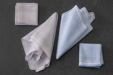 Folded blue and beige handkerchiefs arranged on a dark background, showcasing classic men's...