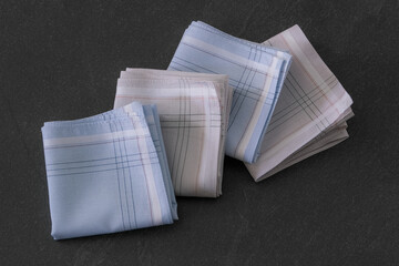 Folded blue and beige handkerchiefs arranged on a dark background, showcasing classic men's...