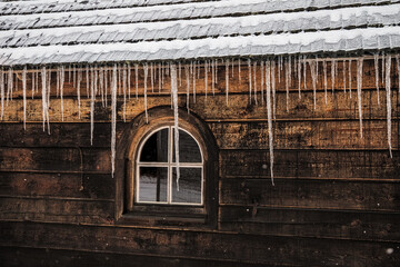 Naklejka premium Icicles hanging from snowy roof of wooden house in Czech Republic