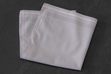 Folded beige handkerchief arranged on a dark background, showcasing classic men's accessories in a clean, elegant style.