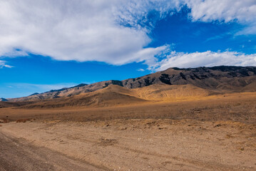 Dirt road crossing dry fields leading to mountains in Idaho under blue sky