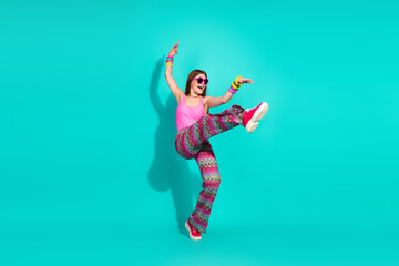 Cheerful woman in bright retro attire dancing joyfully on a vibrant turquoise background embodying...