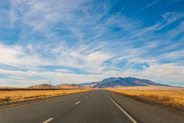 Open road crossing Nevada desert landscape towards mountains under blue sky